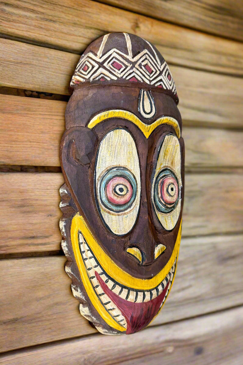 Colorful hand-carved wooden tribal mask with a wide yellow smile and geometric patterns mounted on wooden planks